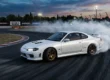 Nissan Silvia S15 branco fazendo drift em uma pista de corrida durante o entardecer, com fumaça saindo dos pneus traseiros.