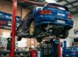 Subaru Impreza WRX azul clássico elevado em um elevador hidráulico dentro de uma oficina especializada em modificação automotiva.