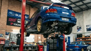 Subaru Impreza WRX azul clássico elevado em um elevador hidráulico dentro de uma oficina especializada em modificação automotiva.