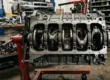 Fotografia técnica em close detalhando os mancais e cilindros usinados de um bloco de motor japonês de ferro fundido em uma oficina.