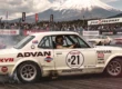 Corrida antiga no circuito de Fuji com um Nissan Skyline Hakosuka pilotado por Kunimitsu Takahashi deslizando de lado com fumaça nos pneus.