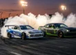 Dois carros de drift profissionais fazendo tandem em alta velocidade com pneus soltando fumaça densa na pista.
