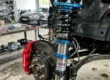 Conjunto de suspensão coilover ajustável com corpo rosqueado e molas esportivas instalado na caixa de roda de um carro de alta performance.