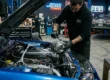 Mecânico especializado realizando manutenção no cofre do motor de um carro JDM clássico em oficina de performance.