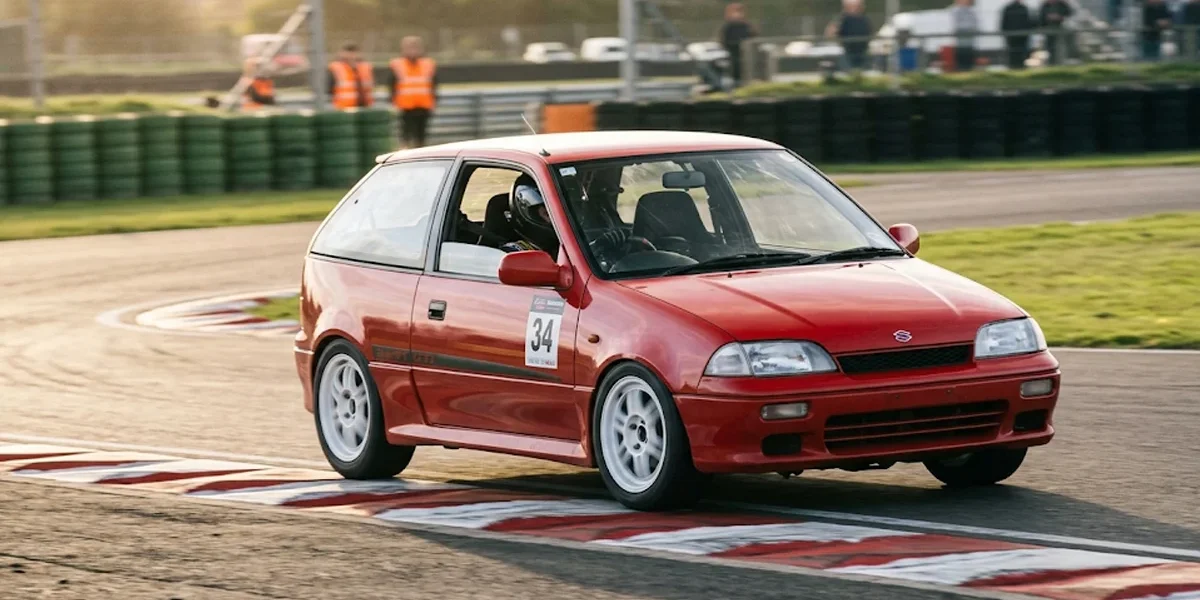 Fotografia em movimento de um Suzuki Swift GTi vermelho atacando a zebra em uma curva de autódromo.