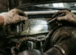 Mecânico iluminando com lanterna a numeração do chassi no cofre do motor durante vistoria cautelar automotiva.
