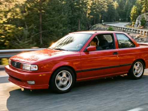 Nissan Sentra SE-R B13 vermelho em movimento em uma estrada sinuosa ao entardecer.